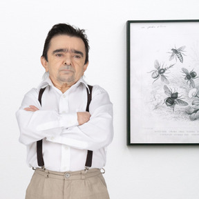 A man standing with arms crossed next to a picture on the wall
