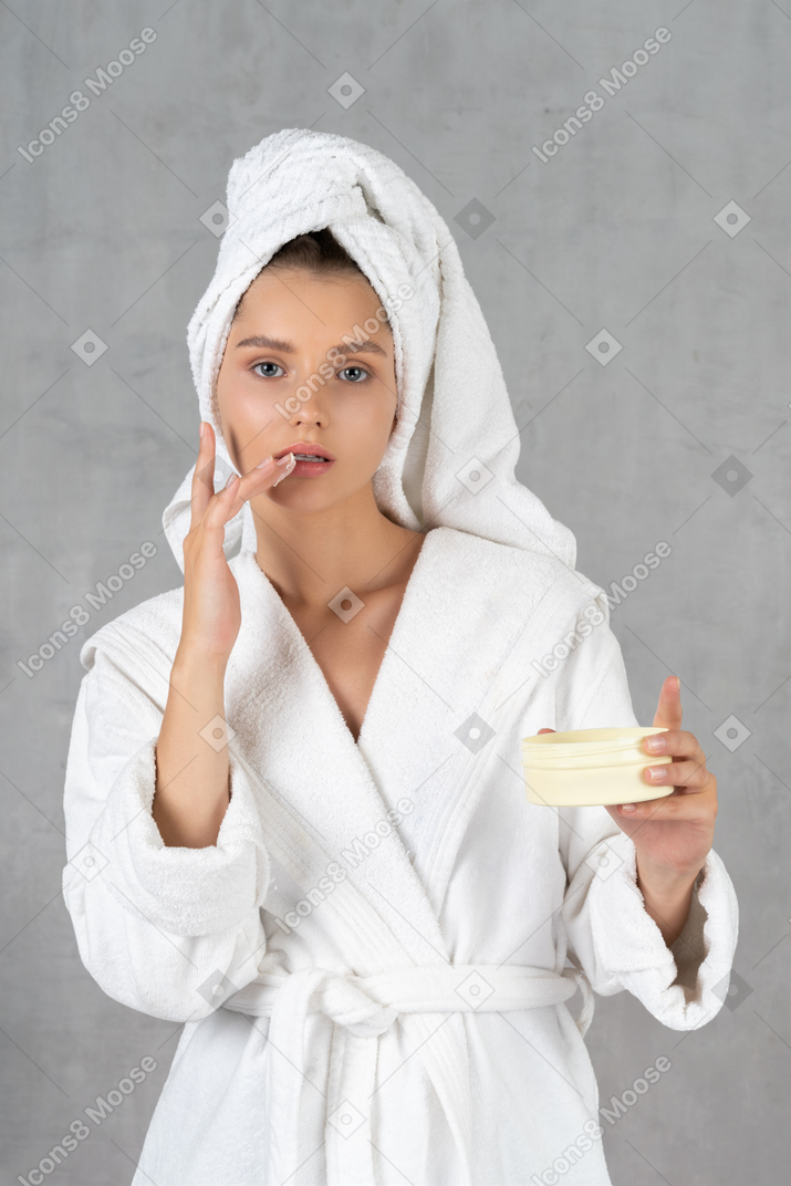Mujer en bata de baño aplicando crema en el labio