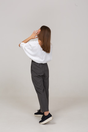 Dreiviertel-rückansicht einer jungen dame in bürokleidung, die ihr gesicht berührt