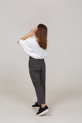 Three-quarter back view of a young lady in office clothing touching her face