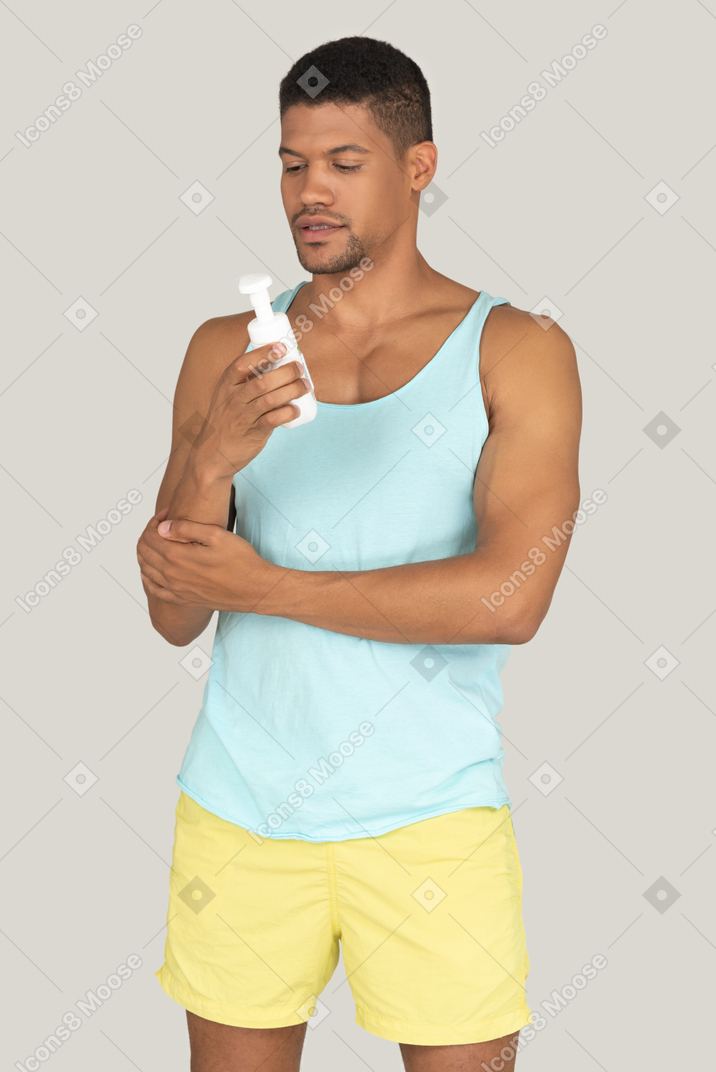 Man in ank top and shorts holdiing bottle of cream