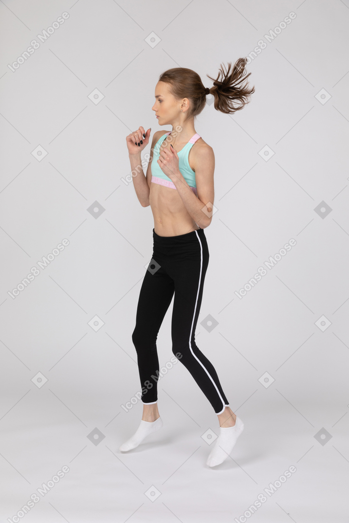 Side view of a teen girl in sportswear stepping forward while clenching fists