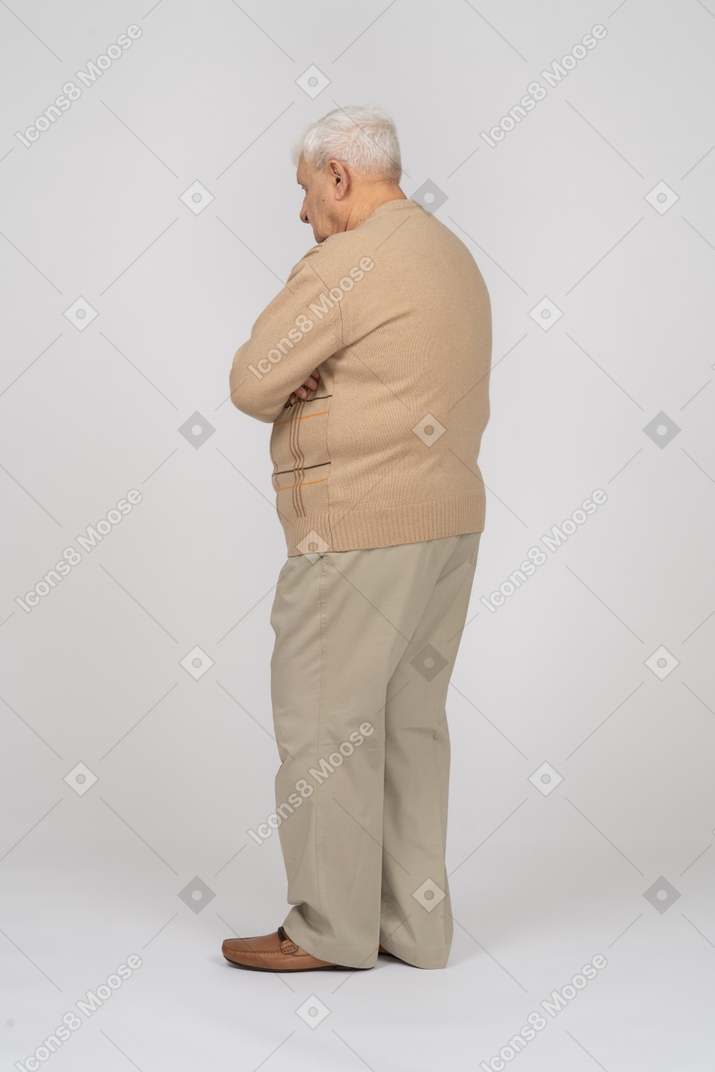 Side view of an old man in casual clothes standing with crossed arms
