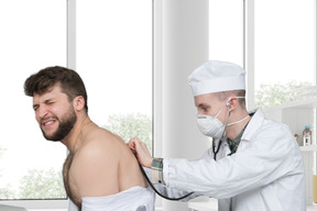 A man in a white lab coat is listening to a man with stethoscope