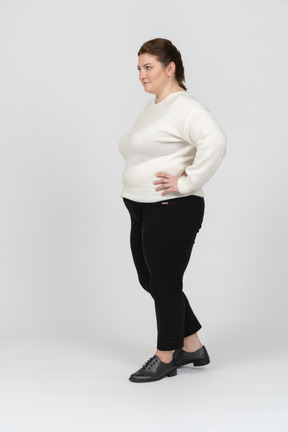 腰に手を当てて立っている白いセーターのプラスのサイズの女性