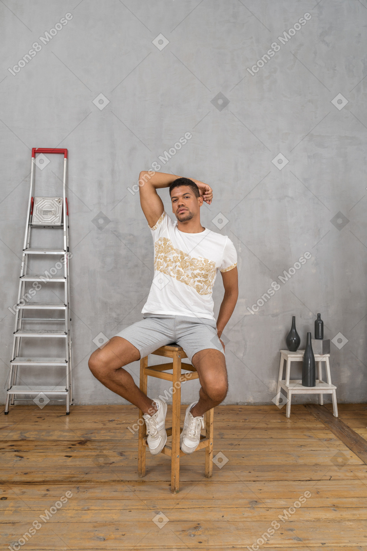 Young man sitting on chair with one arm raised overhead