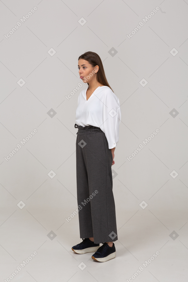 Dreiviertelansicht einer jungen dame in bürokleidung, die hände hinter sich hält und zunge zeigt
