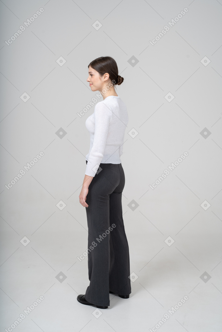 Вид сбоку на молодую женщину в белом свитере и черных брюках