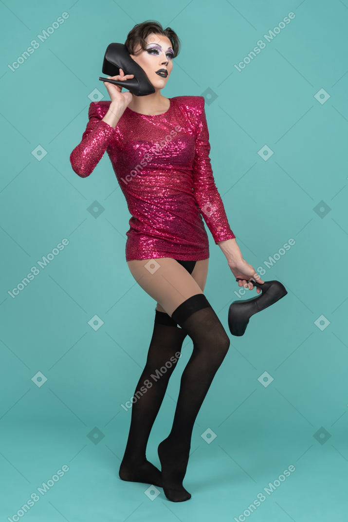 Drag queen in pink dress pretending to use their shoe as a phone