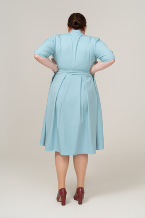 Rear view of a woman in blue dress standing with hands on hips