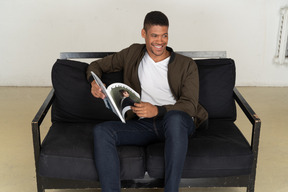 Красивый молодой человек сидит на диване и держит журнал