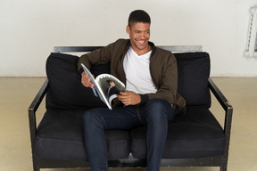 Beautiful young man sitting on a sofa and holding a magazine