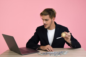 Cara jovem bonito falando no laptop e segurando uma moeda nem