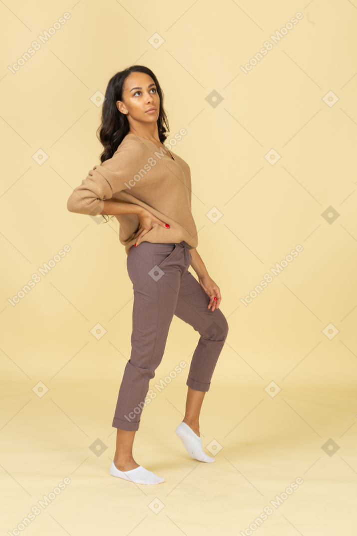 Side view of a dark-skinned young lady putting hand on hip while looking aside
