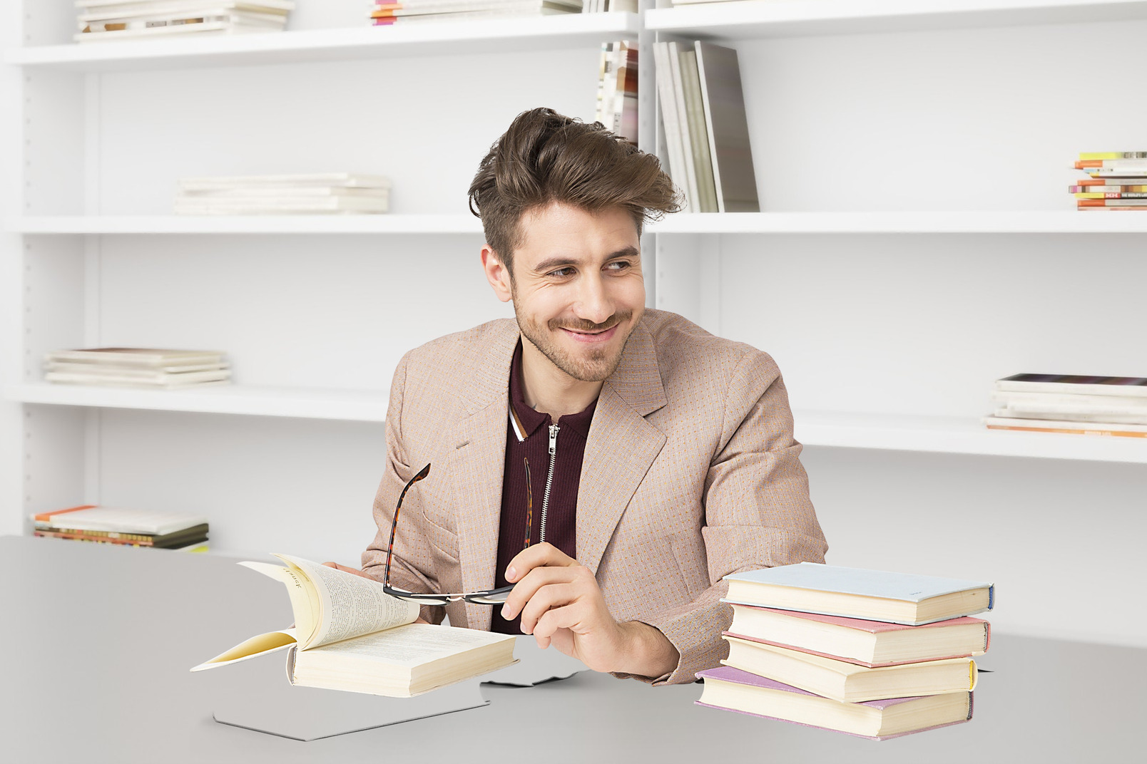 A man in a suit sits at a desk with a stack of books
