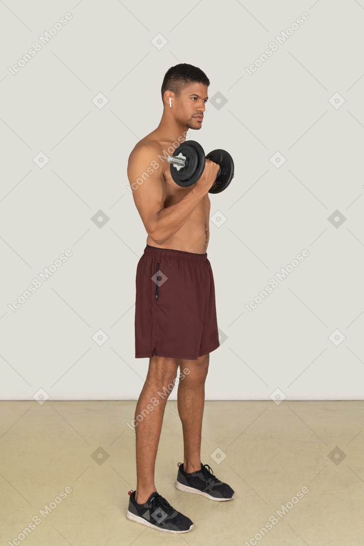 Vista de tres cuartos de un apuesto hombre atlético haciendo ejercicios con mancuernas
