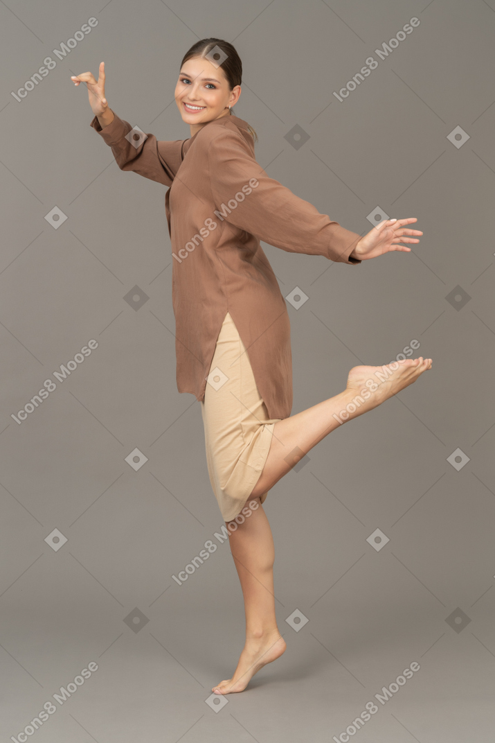 Vista laterale di una donna in piedi a piedi nudi in punta di piedi con la gamba sollevata