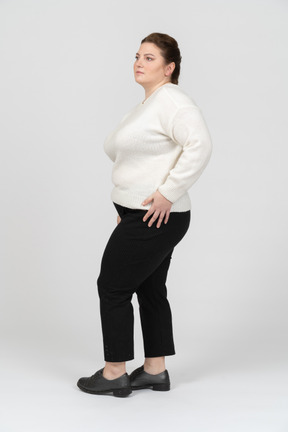 Пухлая женщина в белом свитере стоит с руками за головой