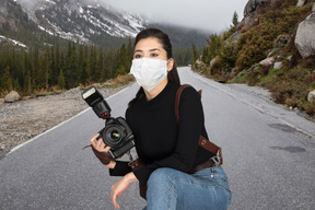 A woman holding a camera and wearing a face mask