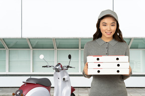 Woman holding pizza boxes next to delivery scooter