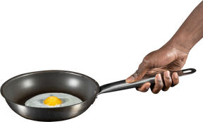 Человеческая рука держит жареное яйцо на сковороде