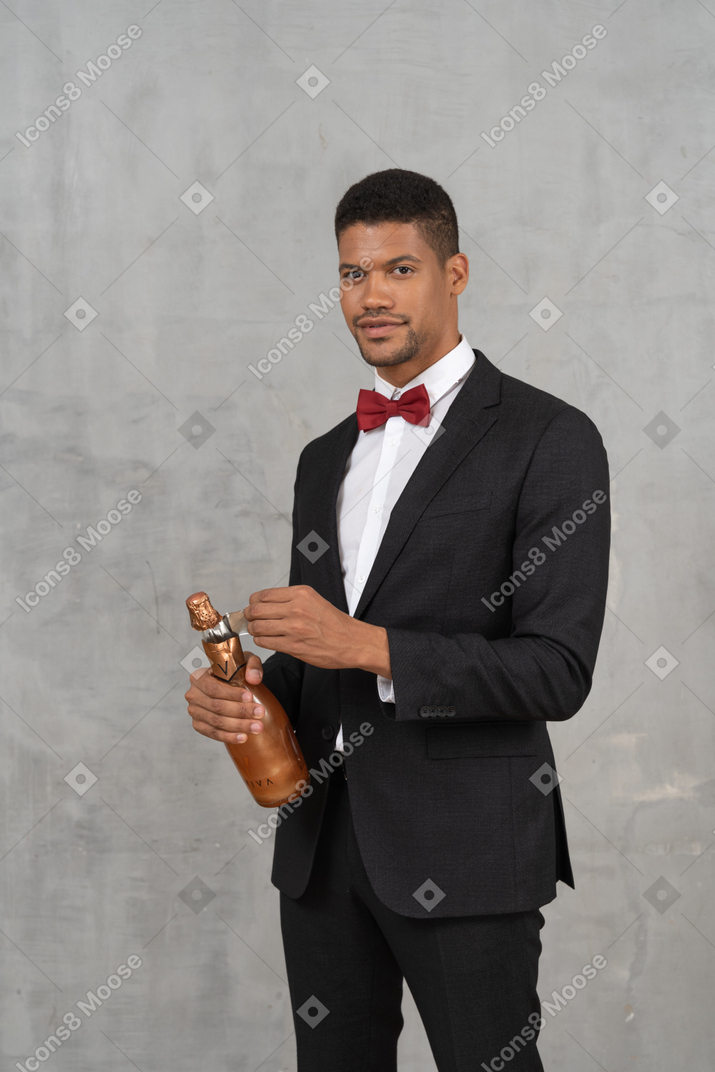 Uomo in giacca e cravatta che rimuove l'involucro di alluminio dalla bottiglia di champagne
