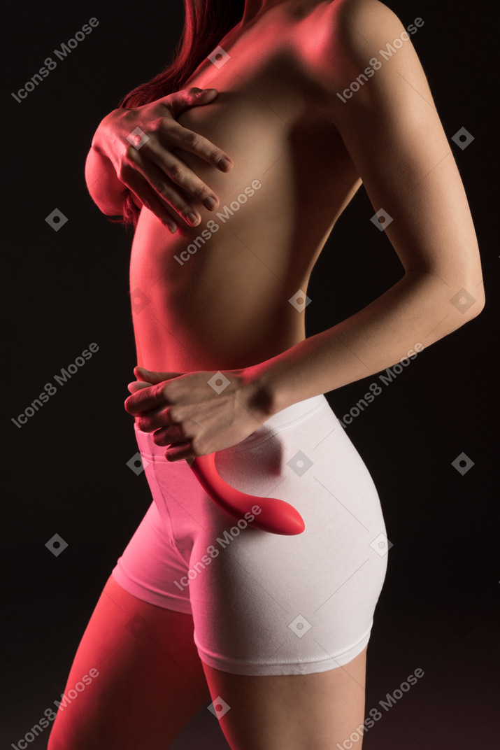 Vue latérale d'une jeune femme nue sensuelle en boxer couvrant la poitrine avec la main et tenant un jouet sexuel