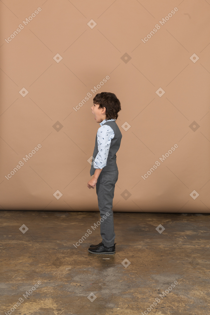 Вид сбоку на мальчика в костюме, стоящего с открытым ртом