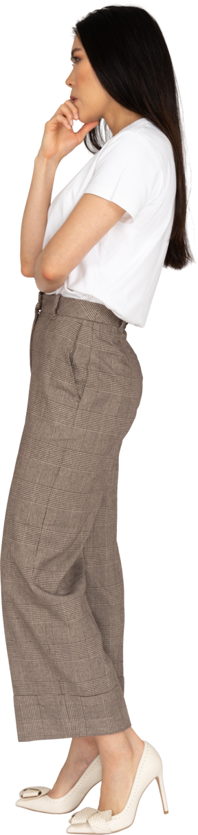 Vista laterale di una giovane donna premurosa in calzoni e t-shirt toccando il mento