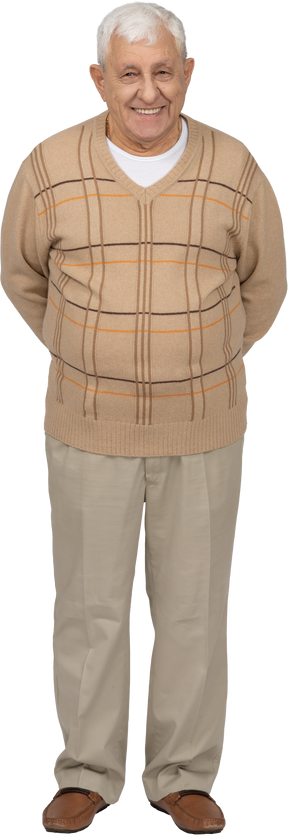 Vista frontal de un anciano feliz con ropa informal de pie con las manos detrás de la espalda y mirando a la cámara