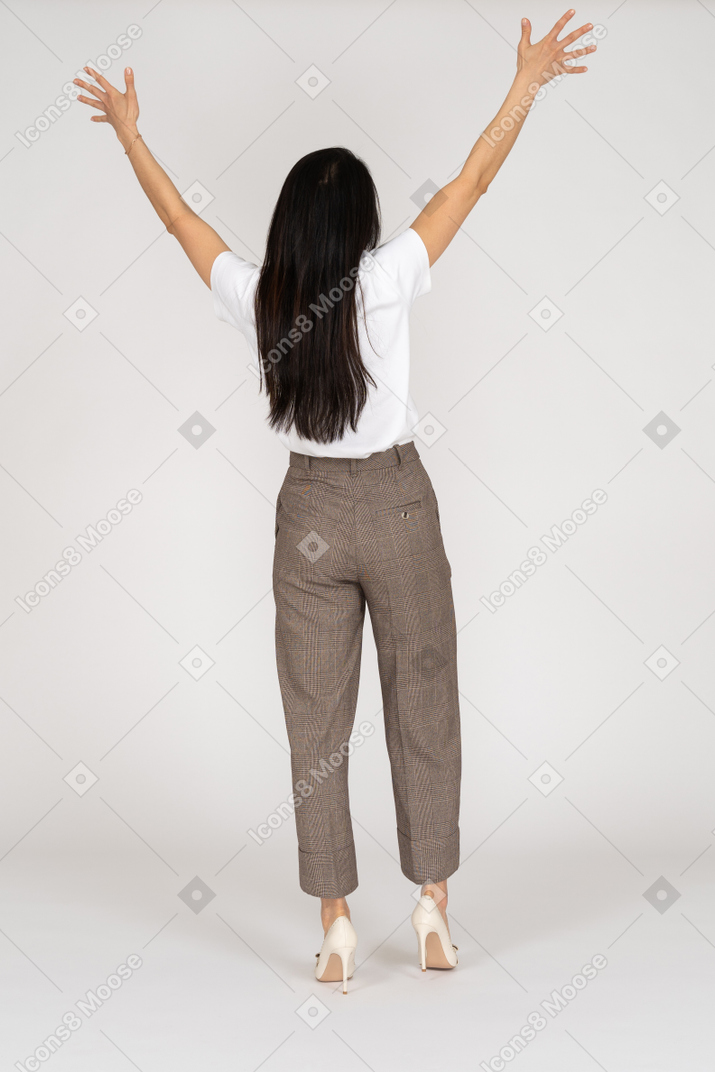 Vista traseira de uma jovem de calça e camiseta levantando as mãos