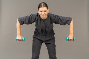 Вид спереди молодой женщины в комбинезоне, делающей упражнения с гантелями
