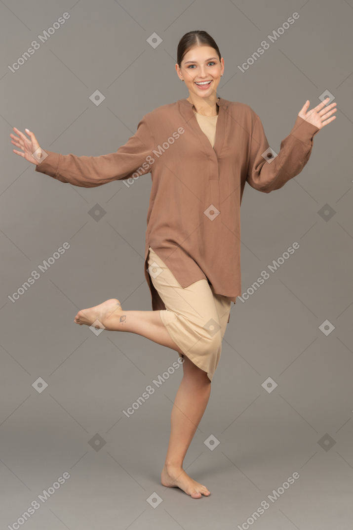 Vue de face d'une jeune femme debout pieds nus sur une jambe avec les bras grands ouverts
