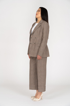 Three-quarter view of a confused young lady in brown business suit leaning back