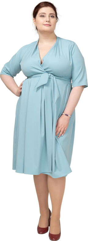 Vue de face d'une femme en robe bleue posant avec la main sur la hanche
