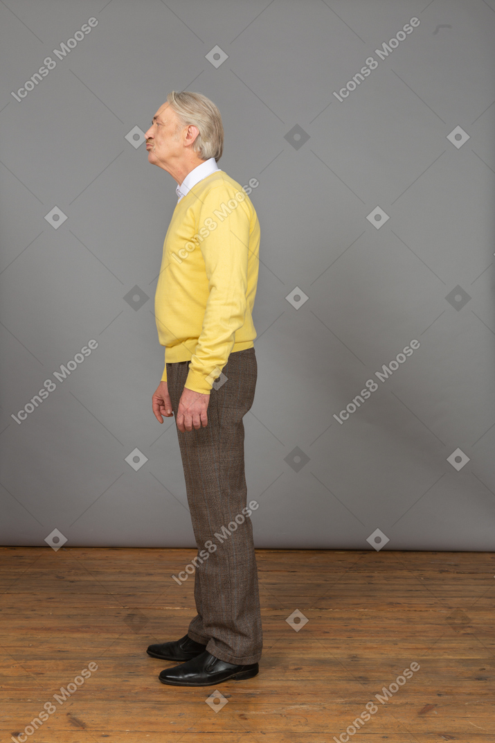 Side view of a sad old man wearing yellow pullover and looking aside