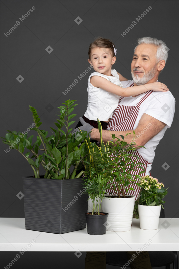 A mature man holding a little girl on his hands next to the house plants