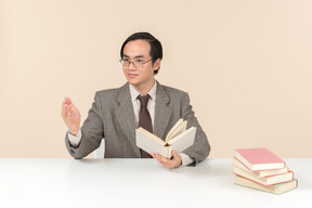 Um professor asiático de terno xadrez, gravata e livro na mão, trabalhando com a turma