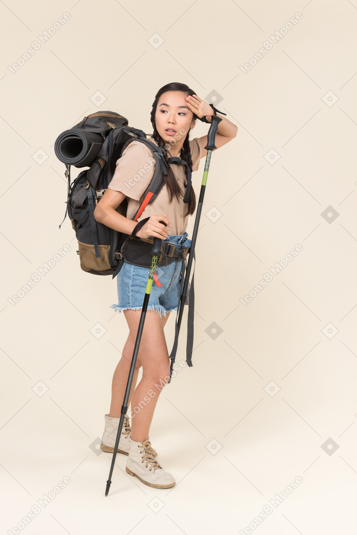 Tired hiker woman walking using trekking poles and drying her forehead with hand