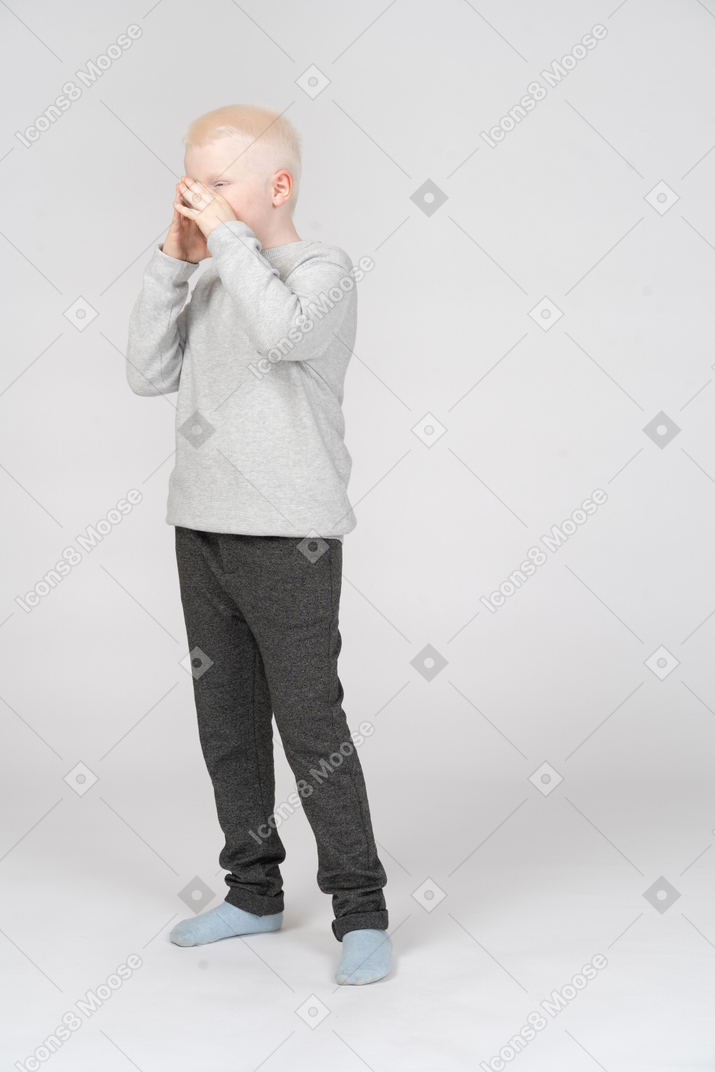 Вид в три четверти на мальчика, закрывающего рот руками