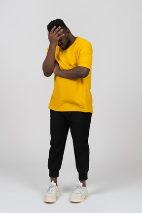 Vorderansicht eines beschämten jungen dunkelhäutigen mannes im gelben t-shirt, das gesicht versteckt