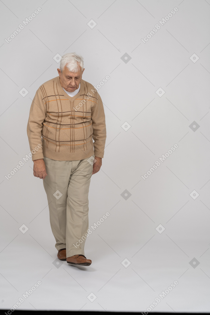 Vista frontal de un anciano con ropa informal caminando y mirando hacia abajo