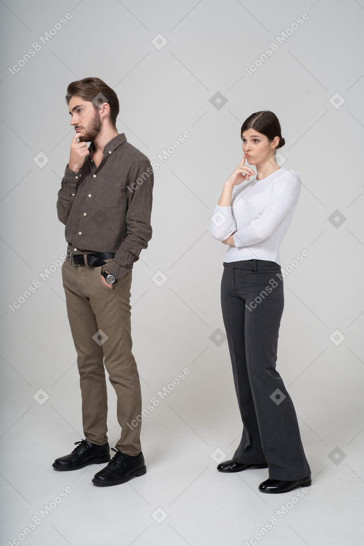 Vista de tres cuartos de una pareja joven pensativa en ropa de oficina tocando la barbilla