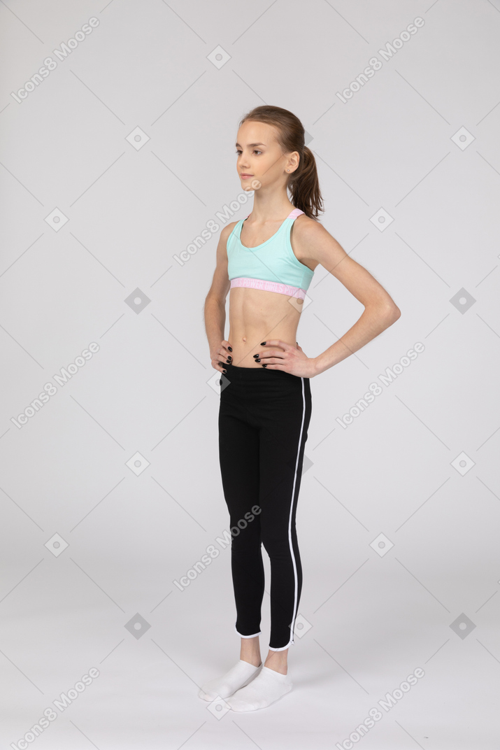 Vista de tres cuartos de una jovencita en ropa deportiva poniendo las manos en las caderas