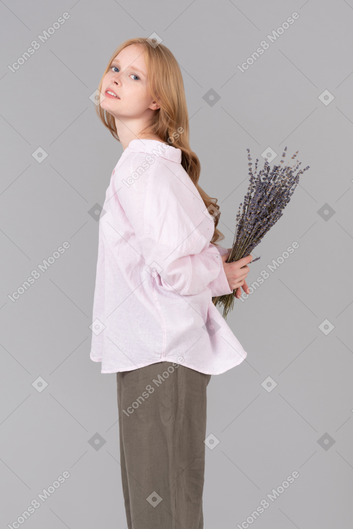 Young woman holding bunch of flowers behind her back