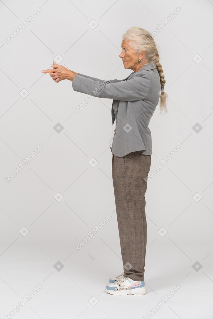 Seitenansicht einer alten dame im anzug, die eine waffe mit den fingern zeigt