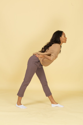 Side view of a dark-skinned young female putting hand on hip while leaning forward