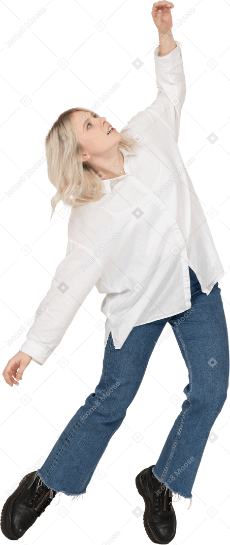 Front view of a blonde female in casual clothes dancing on her tiptoes and raising hand while looking up