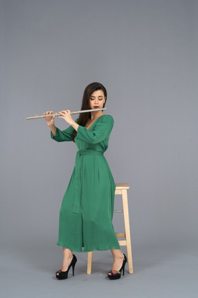 Full-length of a young lady in green dress sitting on a chair while playing the clarinet