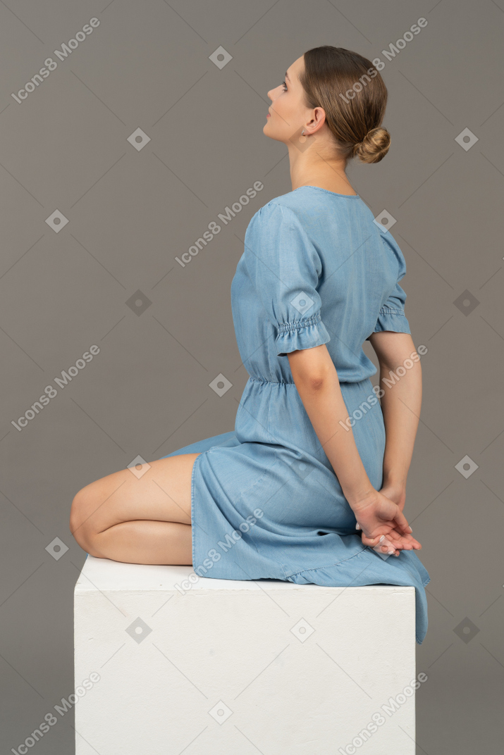 坐在立方体上的穿着蓝色连衣裙的年轻女子的背面视图